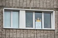 Child stands on window behind banner with inscription Stay at home, looks to right