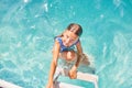 A child on the steps climbing out of the pool, little girl having fun in the swimming pool,