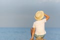 Child in a straw hat sitting on beach and looking at the distance. Back view Royalty Free Stock Photo