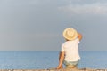 Child in a straw hat sitting on beach and looking at the distance. Holidays. Back view Royalty Free Stock Photo