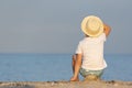 Child in a straw hat sitting on beach and looking at sea. Back view Royalty Free Stock Photo