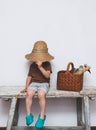 Child in straw hat sitting on a bench with gardening tools in basket. Small gardener, farmer. Small helper. Royalty Free Stock Photo