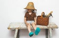 Child in straw hat sitting on a bench with gardening tools in basket. Small gardener, farmer. Small helper. Royalty Free Stock Photo