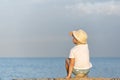 Child in straw hat sitting at sunset on the beach and looks at sea Royalty Free Stock Photo