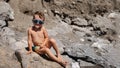 A child in sunglasses is sitting and sunbathing on large boulders, on the beach near the sea. Royalty Free Stock Photo