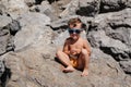 A child in sunglasses is sitting and sunbathing on large boulders, on the beach near the sea. Royalty Free Stock Photo