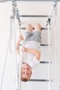 A child on the Swedish wall plays sports at home, a boy climbs a ladder with a rope, the concept of sports and health