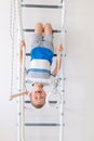 A child on the Swedish wall plays sports at home, a boy climbs a ladder with a rope, the concept of sports and health