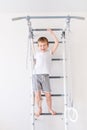 A child on the Swedish wall plays sports at home, a boy climbs a ladder with a rope, the concept of sports and health