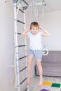 A child on the Swedish wall plays sports at home, a boy climbs a ladder with a rope, the concept of sports and health