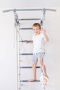 A child on the Swedish wall plays sports at home, a boy climbs a ladder with a rope, the concept of sports and health