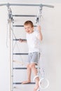 A child on the Swedish wall plays sports at home, a boy climbs a ladder with a rope, the concept of sports and health