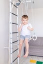 A child on the Swedish wall plays sports at home, a boy climbs a ladder with a rope, the concept of sports and health