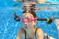 Child swims in pool underwater, happy active girl in goggles has fun in water