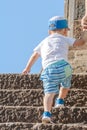 The child in a T-shirt, shorts and a cap goes up the stairs. Picture taken from the back