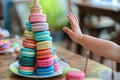 child at a table with a colorful macaron tower, reaching out