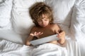 Child with tablet in bed. Little boy lying on sofa watching movie on tablet, in living room, Parental permission, safety