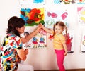 Child with teacher draw paints in playroom.