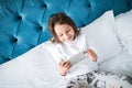 Child, technology and internet concept - little girl lying in bed with smartphone playing games at home