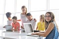 Child with technology tablet and laptop computer in classroom teacher on the background Royalty Free Stock Photo