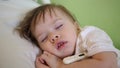 Child temperature is measured with thermometer in hospital ward. close-up. Baby sleeps in hospital ward on a white bed.