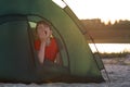 Child in tent yawns. Morning at campsite. Children`s tourism, camping travel