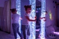 Child in therapy sensory stimulating room, snoezelen. Autistic child interacting with colored bubble tube lamp during therapy.