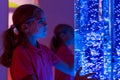 Child in therapy sensory stimulating room, snoezelen. Child interacting with colored lights bubble tube lamp during therapy.