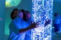 Child in therapy sensory stimulating room, snoezelen. Child interacting with colored lights bubble tube lamp during therapy. Royalty Free Stock Photo