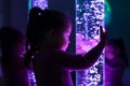 Child in therapy sensory stimulating room, snoezelen. Child interacting with colored lights bubble tube lamp during therapy. Royalty Free Stock Photo