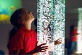 Child in therapy sensory stimulating room, snoezelen. Child interacting with colored lights bubble tube lamp during therapy.