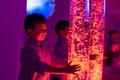 Child in therapy sensory stimulating room, snoezelen. Child interacting with colored lights bubble tube lamp during therapy. Royalty Free Stock Photo