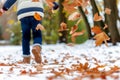 child throwing autumn leaves in air, snowcovered ground beneath