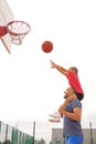 A child throws a ball into basketball hoop, sitting on his father's shoulders Royalty Free Stock Photo