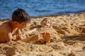 Child, tickling sibling on the beach on the feet with feather, kid cover in sand, smiling, laughing