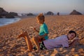 Child, tickling sibling on the beach on the feet with feather, kid cover in sand, smiling, laughing Royalty Free Stock Photo