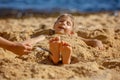 Child, tickling sibling on the beach on the feet with feather, kid cover in sand, smiling, laughing