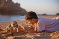 Child, tickling sibling on the beach on the feet with feather, kid cover in sand, smiling, laughing