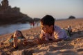 Child, tickling sibling on the beach on the feet with feather, kid cover in sand, smiling, laughing