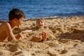 Child, tickling sibling on the beach on the feet with feather, kid cover in sand, smiling, laughing