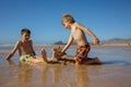 Child, tickling sibling on the beach on the feet with feather, kid cover in sand, smiling, laughing