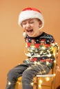 The child tied with a garlands sits on the chair. Orange background. Vertical photo.