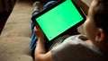 Child tilting to the left a tablet PC with green screen, back view