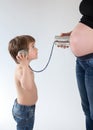 Child trying to listen inside the belly of a pregnant woman with a tin can phone Royalty Free Stock Photo