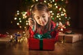 A child unties the ribbon on a gift box on Christmas night lying on the floor in the semi-darkness at the Christmas tree with colo Royalty Free Stock Photo