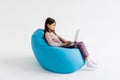 Child using laptop while resting on bean bag chair isolated on white background Royalty Free Stock Photo