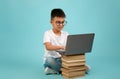 Child Using Laptop While Sitting on a Stack of Books Against a Light Blue Background Royalty Free Stock Photo