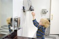 Child using restroom. Little boy dries his hands in the toilet with an automatic dryer. Taking care of the hygiene of children in