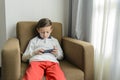 Child sitting in an armchair playing with a smartphone Royalty Free Stock Photo