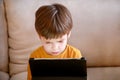 Child using tablet pc on bed at home. Cute boy on sofa is watching cartoon, playing games and learning from laptop. Education, fun Royalty Free Stock Photo